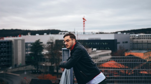 A young man looking over the railing of roof deck.