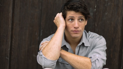 A young man sitting with his back against a wall looking stressed.