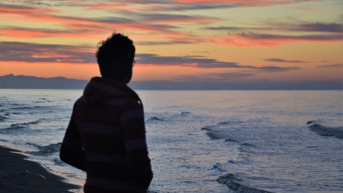 A man looking at a sunset over a body of water.