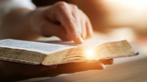 An open Bible with someone's hand pointing to a scripture.