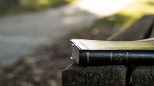 A Bible laying on a park bench.