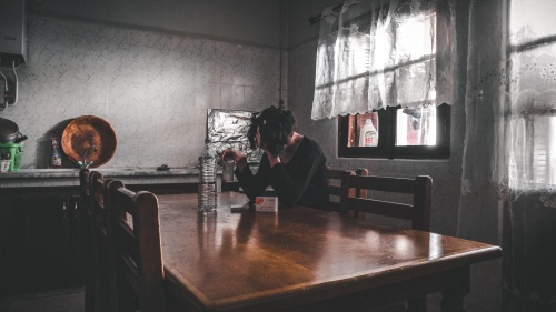 An overwhelmed woman sitting at a kitchen table. 