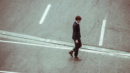 A young man in a suit walking across a road.