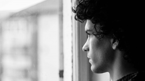 A young man with dark hair staring out a window.