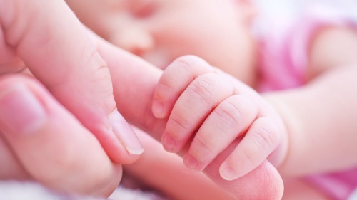 A baby holding the fingers of their mother.