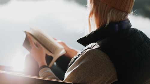 A woman sitting by a lake paging through a Bible.