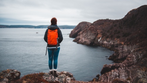 A woman hiking and standing on a cliff over looking a lake.