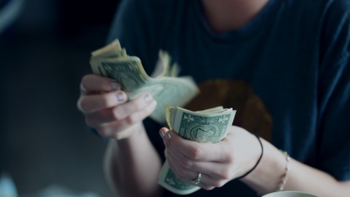 A young woman counting dollar bills.