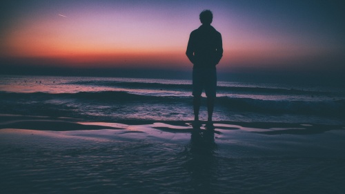 Um homem à beira de um lago ao pôr do sol.