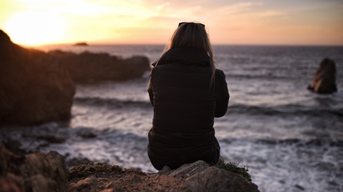 A woman sitting on a rock looking out over water.