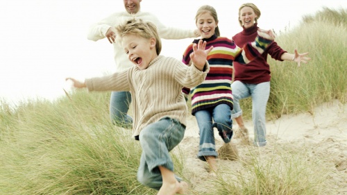 A family running on sandy beach with grass.