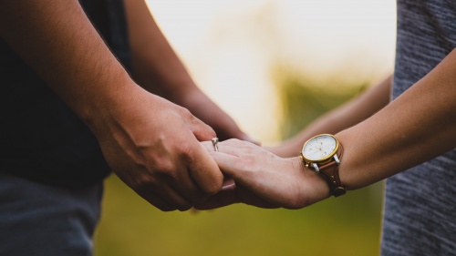 Photo of man and woman with wedding rings holding hands.