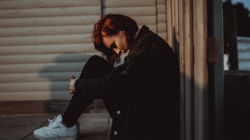 A young woman sitting on the ground hunched over as if she is struggling in life.