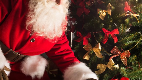 Santa Claus putting Christmas gifts by a tree.