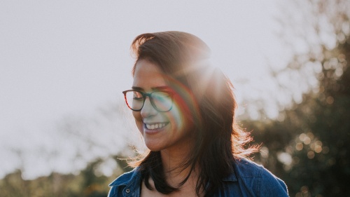 A young woman smiling with sun rays behind her head.