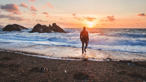 A person walking by water at sunset.