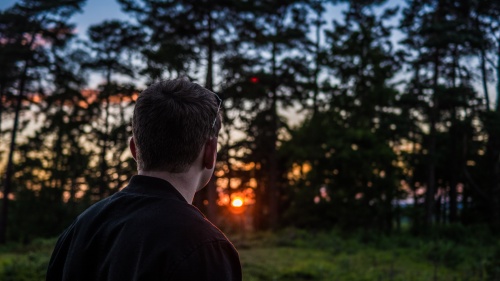 A man outside with the sun behind the trees.