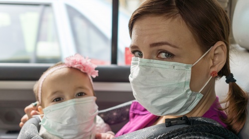 A woman and small child wearing face masks sitting in a car.