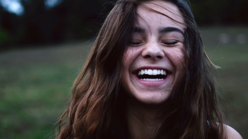 A girl smiling, eyes closed, against an outdoor scene