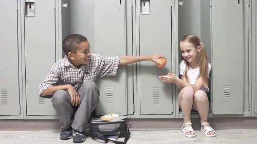 A young boy giving an apple to girl a school.