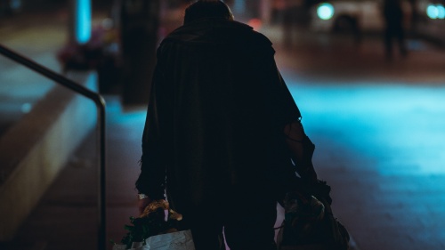 Homeless man walking down street at night under street lights