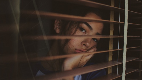 A sad looking woman gazing out a window.