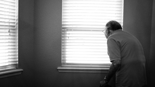 An elderly man looking out a window.