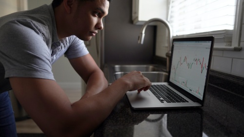 A young man looking at his laptop displaying a graph.