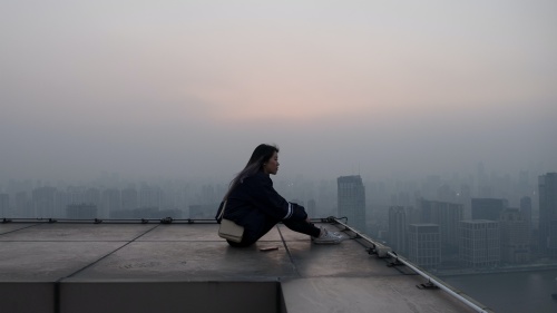 A woman sitting on a rooftop looking out.