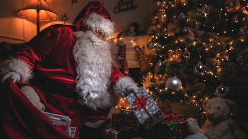 Santa Claus putting gifts under a Christmas tree.