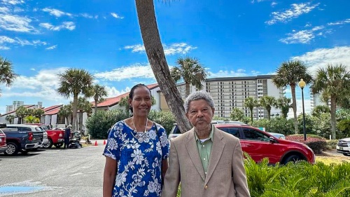 a couple standing outdoors in front of a palm tree