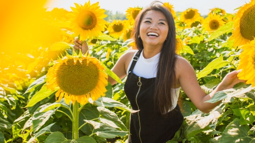 a smiling woman standing in a field of sunflowers
