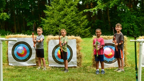 four boys holding bows as they stand in front of archery targets