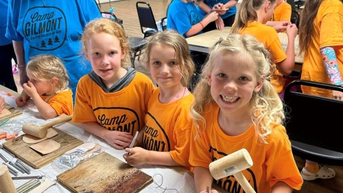 a group of girls seated at a table using leatherworking tools