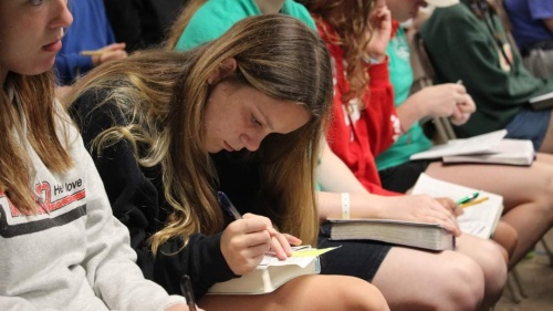 a group of teenagers seated as they read their Bibles