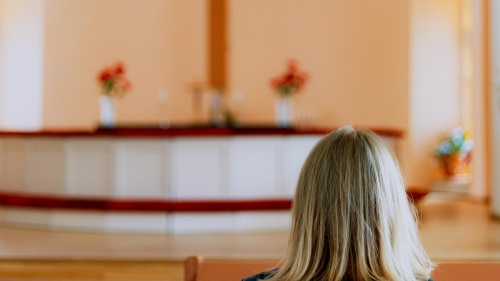 A woman sitting in church looking toward the alter and cross.