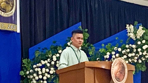 a man standing at a lectern with a blue and floral backdrop