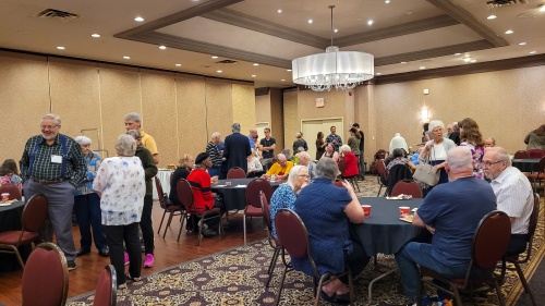 people standing and sitting around circular tables in a banquet room