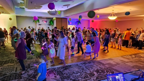 a large group of people dancing in a dimly-lit room with colorful lights and balloons