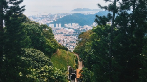 a road cutting through a green landscape towards a foggy cityscape