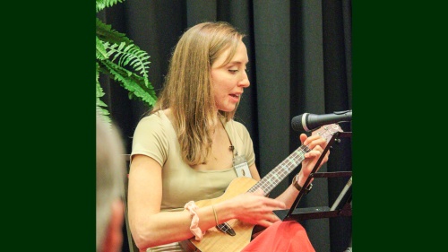 a woman playing a ukulele onstage with a microphone