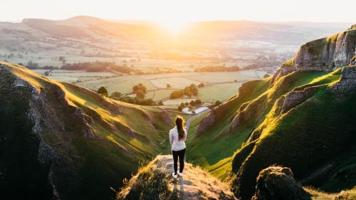 A woman standing on a hill watching the sunrise.