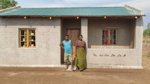 two people standing outdoors in front of a small building with a green roof