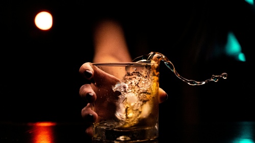 An extended hand holding a beer glass with liquid splashing over the side