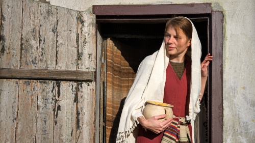 a woman in biblical robes holding a jar and standing in a doorway