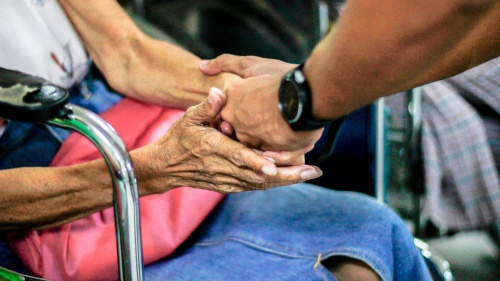 A man holding an older woman's hand sitting in a wheelchair. 
