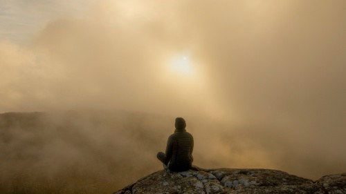 A person sitting on a rock in the morning fog.