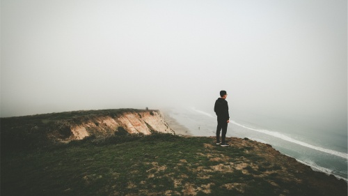 A man looking over a cliff toward the ocean.