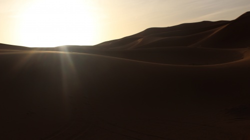 Desert mountains with the bright sun in the distance.