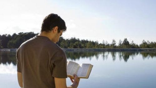 A man reading a Bible outside by a lake.